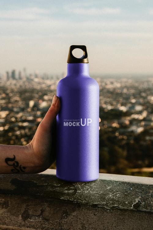 Hand holding a purple stainless steel bottle mockup with urban view - 1198693