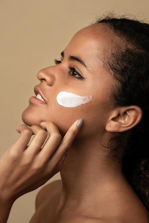 Beautiful African American woman using a moisturizing cream for skincare routine - 2054070