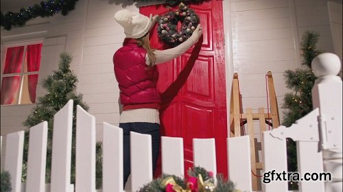 Young woman is decorating the front door of the house with a fur wreath on a christmas eve night christmas colors slow motion dolly shot 2