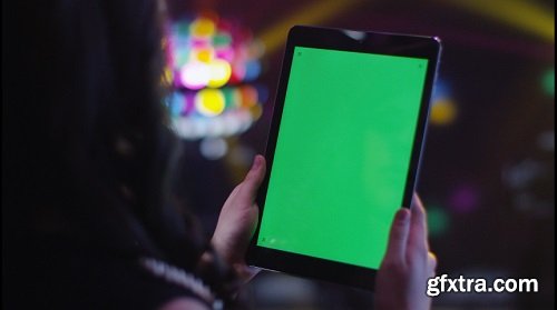 Teen girl is using tablet pc with green screen in portrait mode in nightclub