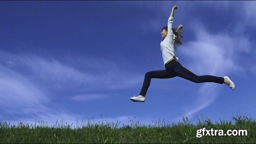 Young happy woman is running and jumping by the camera blue sky and green grass on the background