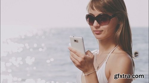 Beautiful young woman in bikini talking smart phone on the sea beach sunny summer by the sea