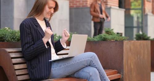 Excited Woman Celebrating Success on Laptop Sitting on Bench