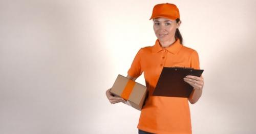 Beautiful Female Courier in Orange Uniform Delivering a Parcel. Light Gray Backround, Studio Shot