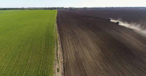 Aerial View of Agricultural Tractors Cultivating Field.