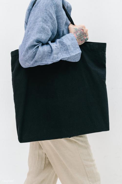 Tattooed woman in a blue linen shirt holding a black tote bag mockup - 1215295
