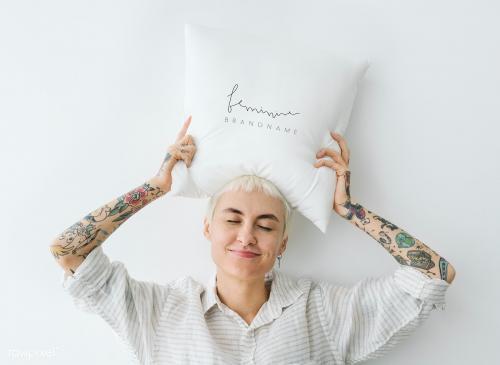 Tattooed woman holding a feminine pillow mockup over her head - 1215299