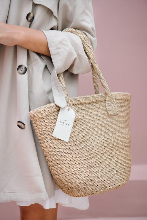 Woman in a beige coat carrying a straw bag with a branding tag mockup - 1215176