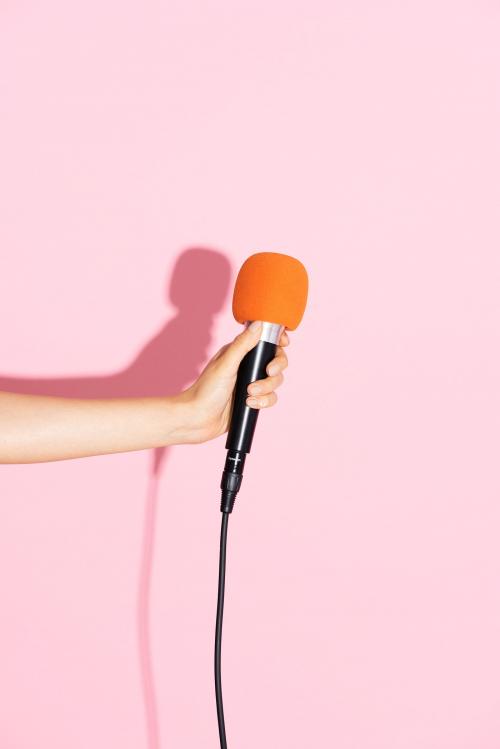 Hand holding a microphone with pink wall - 2050815