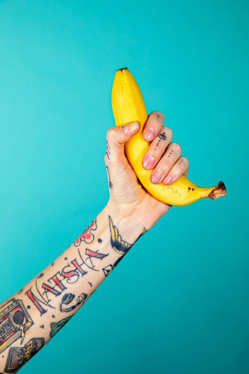 Tattooed hand with a ripe banana on blue background - 2055957