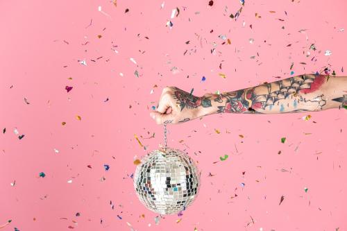 Tattooed hand holding a Christmas disco ball and confetti in the air - 2054416