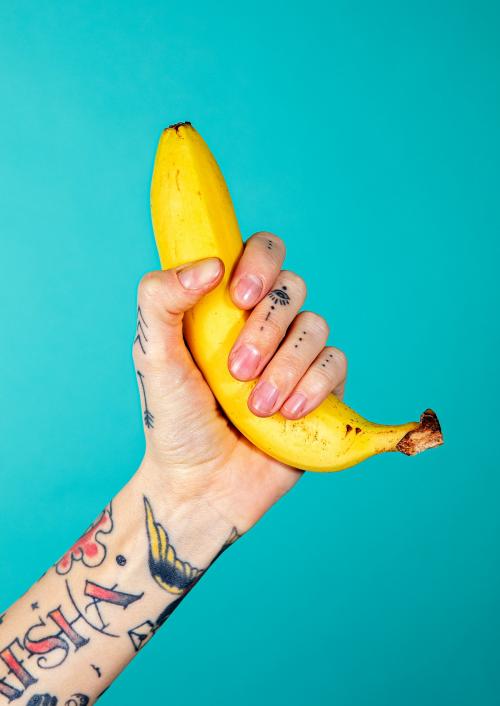 Tattooed hand with a ripe banana on blue background - 2093805