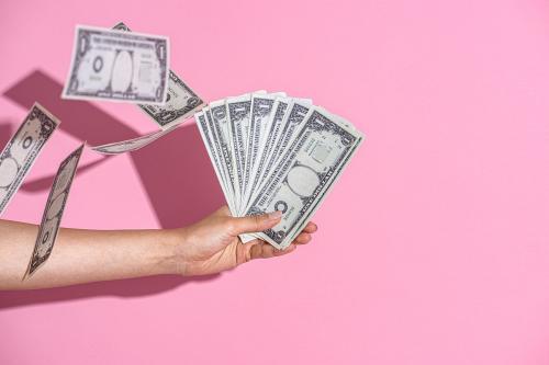 Hand holding cash on a pink wall background - 2054408