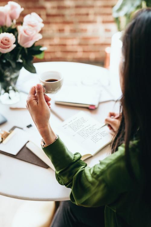 Woman drinking coffee while writing in her journal - 1226519