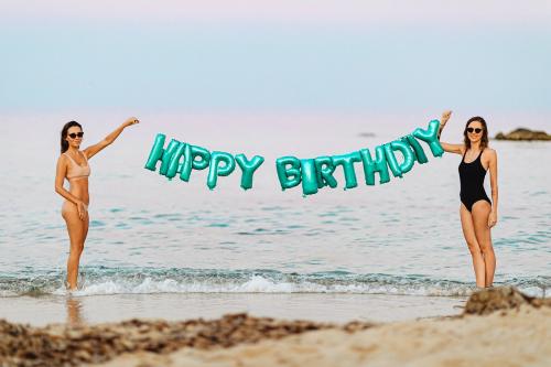 Girls holding a happy birthday foil balloons at the beach - 1228499