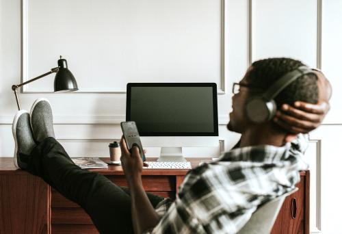 Black man with headphones playing on his phone sitting at his desk - 1224176