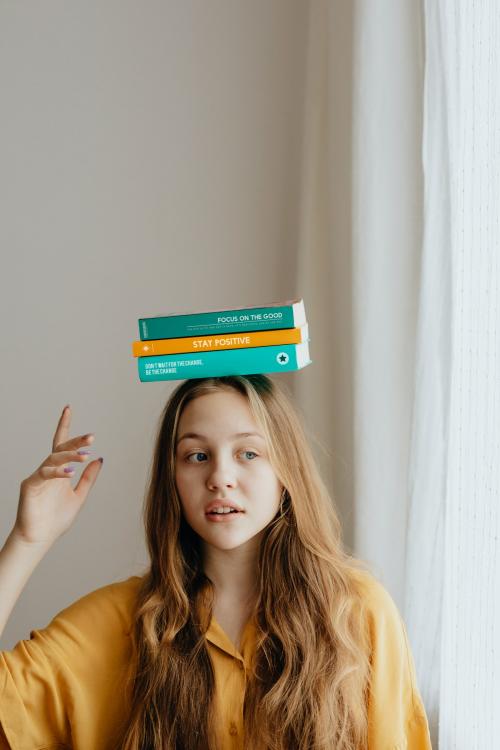 Cheerful blond girl balancing books on her head - 937385