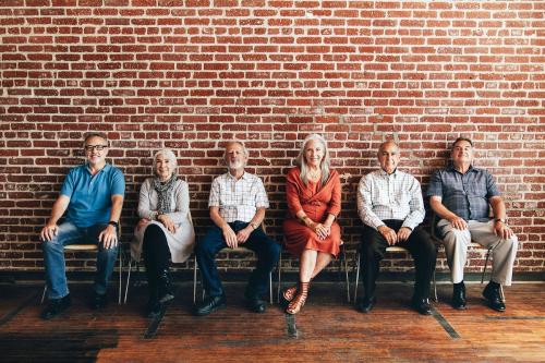 Diverse elderly people sitting in a row against a brick wall background - 1223737
