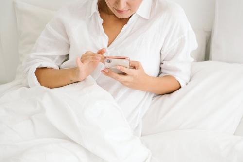 Woman using a phone on her white bed - 1212608