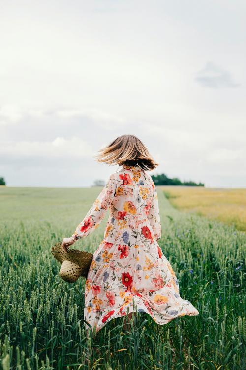 Woman in a floral dress with a woven hat in a field - 1207955