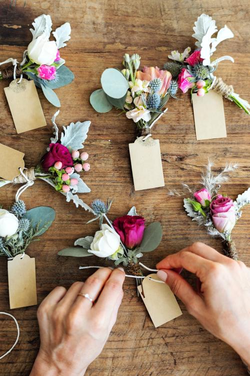 Hands creating boutonnieres with paper tags - 1207509
