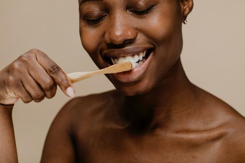Black woman brushing her teeth with a wooden toothbrush - 1203317