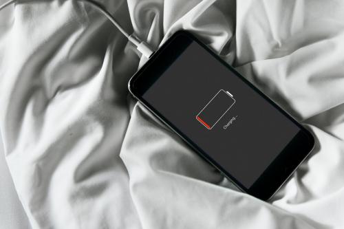 Closeup of out of battery mobile phone charging and lying on white fabric background - 8695