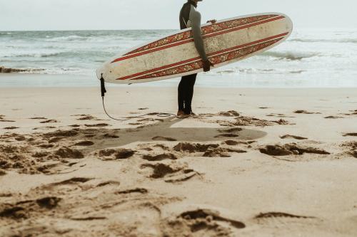 Surfer carrying a surfboard at the beach - 1079962