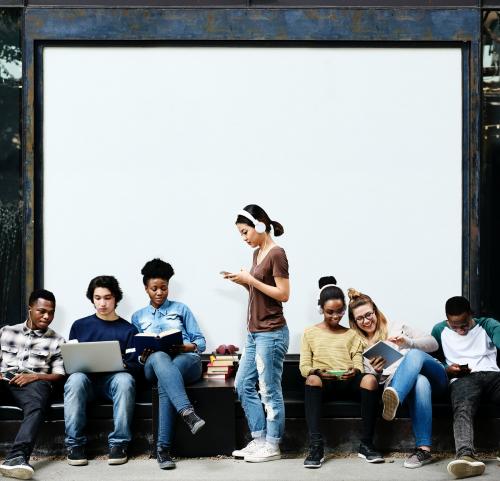 Group of diverse students using digital devices at a bus stop with blank mockup billboard - 6260