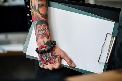 Tattooed hand holding a blank paper clipboard - 6283