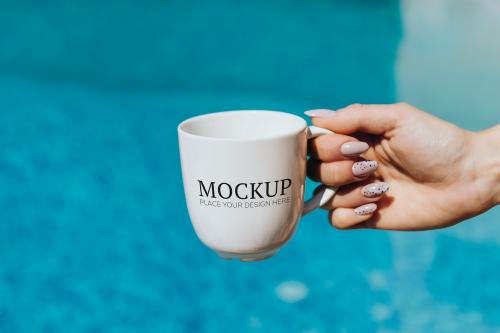 Woman holding a white coffee cup by the pool mockup - 1228513
