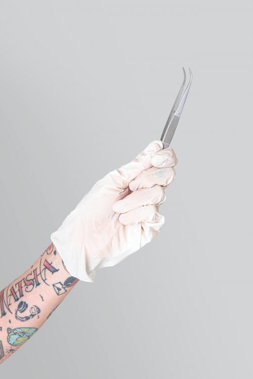 Tattooed hand in a white glove holding a curved tweezers mockup - 2054353