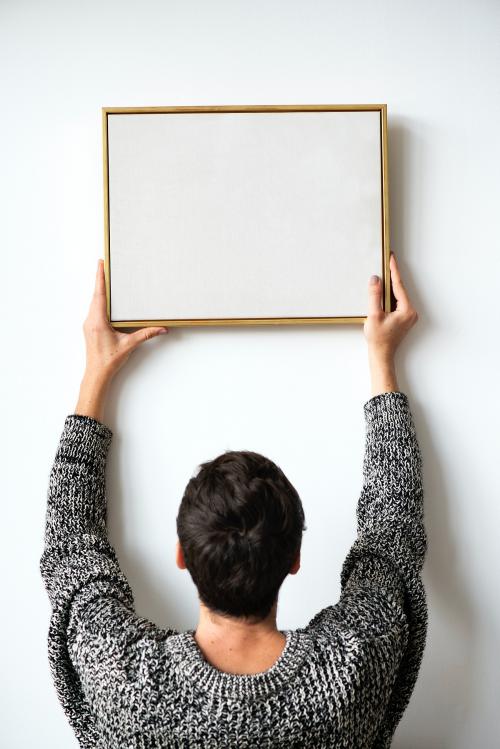 Woman in a black sweater hanging a wooden frame on a white wall mockup - 1231722