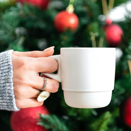 Woman holding a white cup by Christmas tree mockup - 1231827