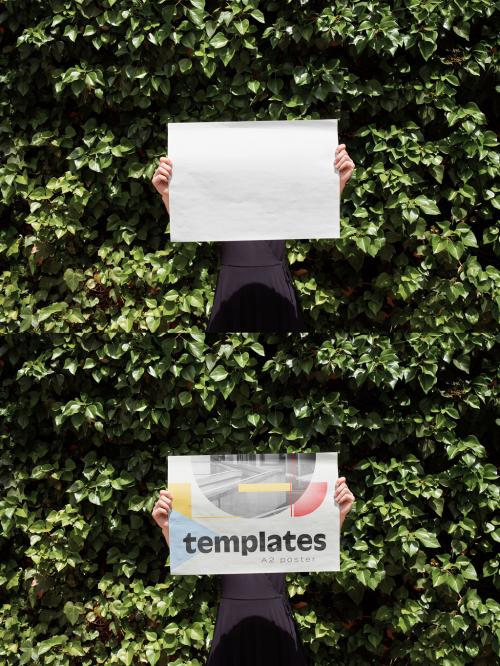 Mockup of person holding customizable A2 horizontal poster in front of face by hedge 649147474