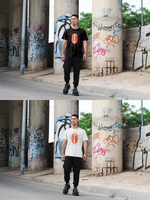 Mockup of man wearing t shirt with customizable color standing by concrete pillars with graffiti 644105536
